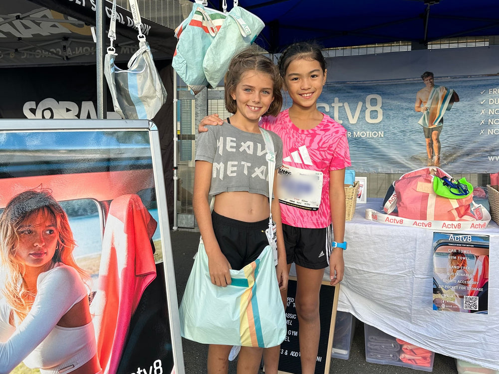 Two young runners at the Actv8 market stall, with Actv8 bags hanging from the tent