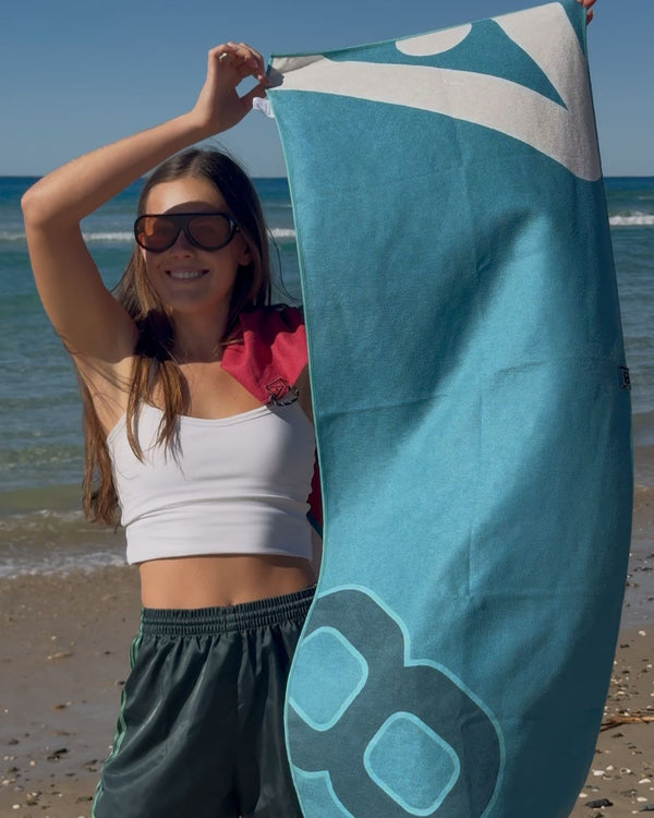 Hoodless Gym Towel in Torque held up full length at the beach