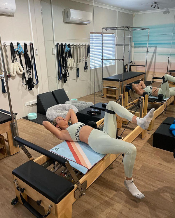 Woman lying on a Pilates reformer with a striped towel under her back