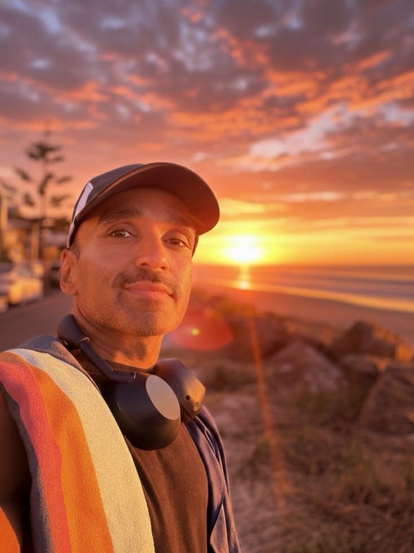 Man in a cap with a striped towel over his shoulder at sunset on the coast