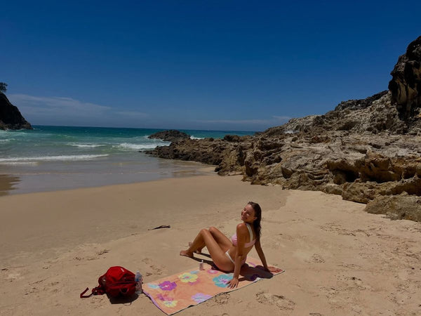 Woman sitting on a floral towel on a quiet beach framed by rocks