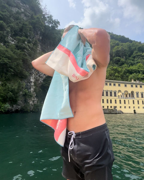 Man drying his hair with a striped towel beside a lake