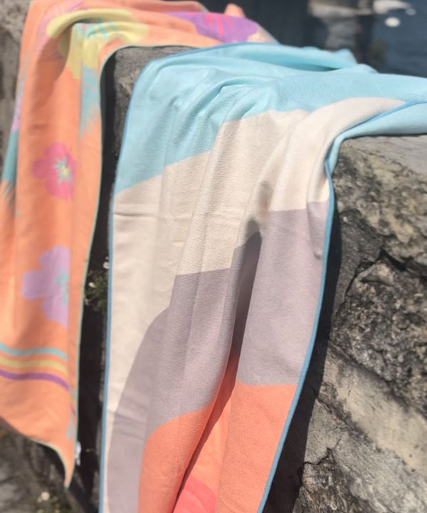 Two patterned towels draped over a stone wall in the sun
